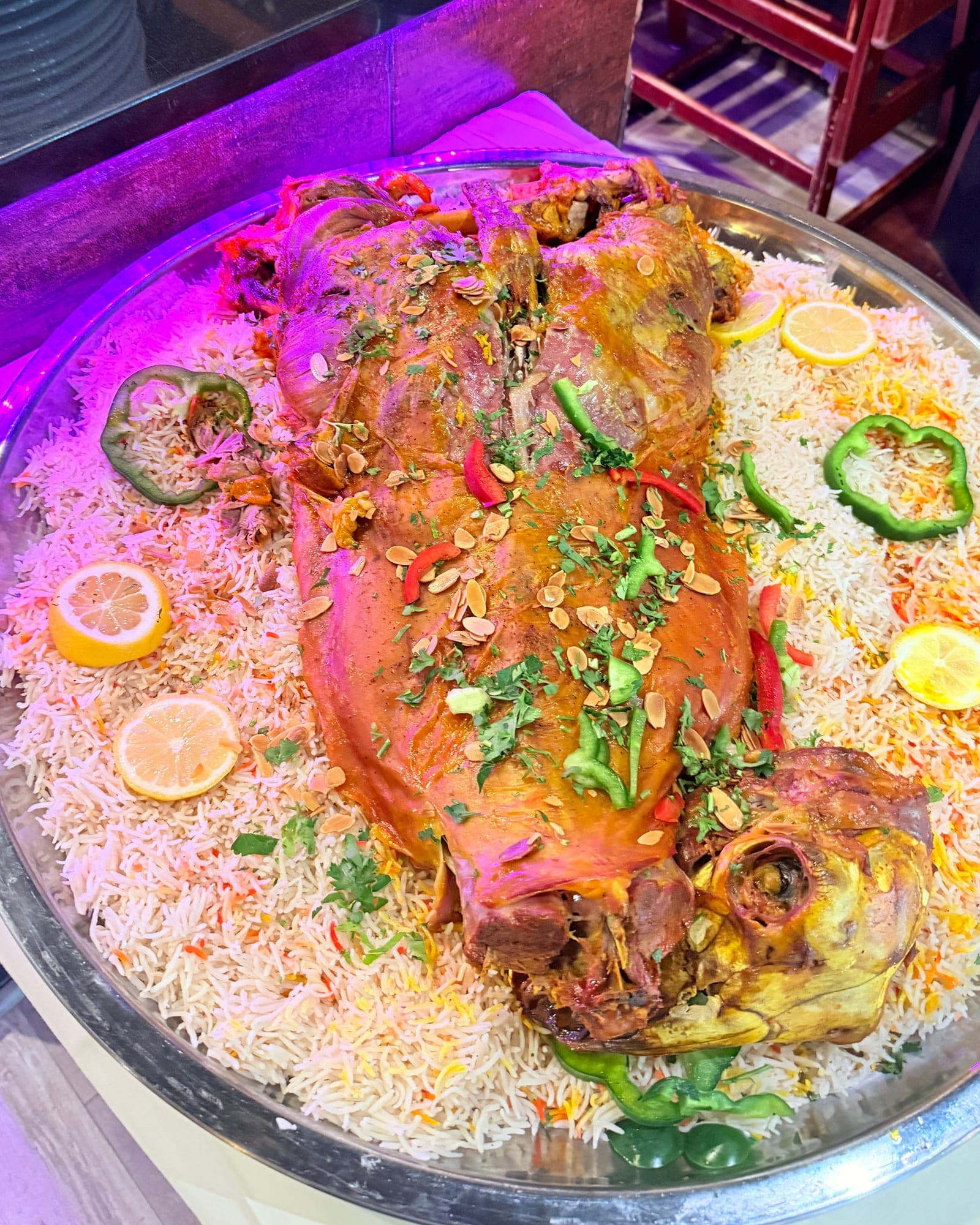 مفطّح: خروف كامل فوق صحن واسع من الرز المبهّر، مزيّن باللوز المحمّص والأعشاب، وحوله الليمون والفلفل الأخضر